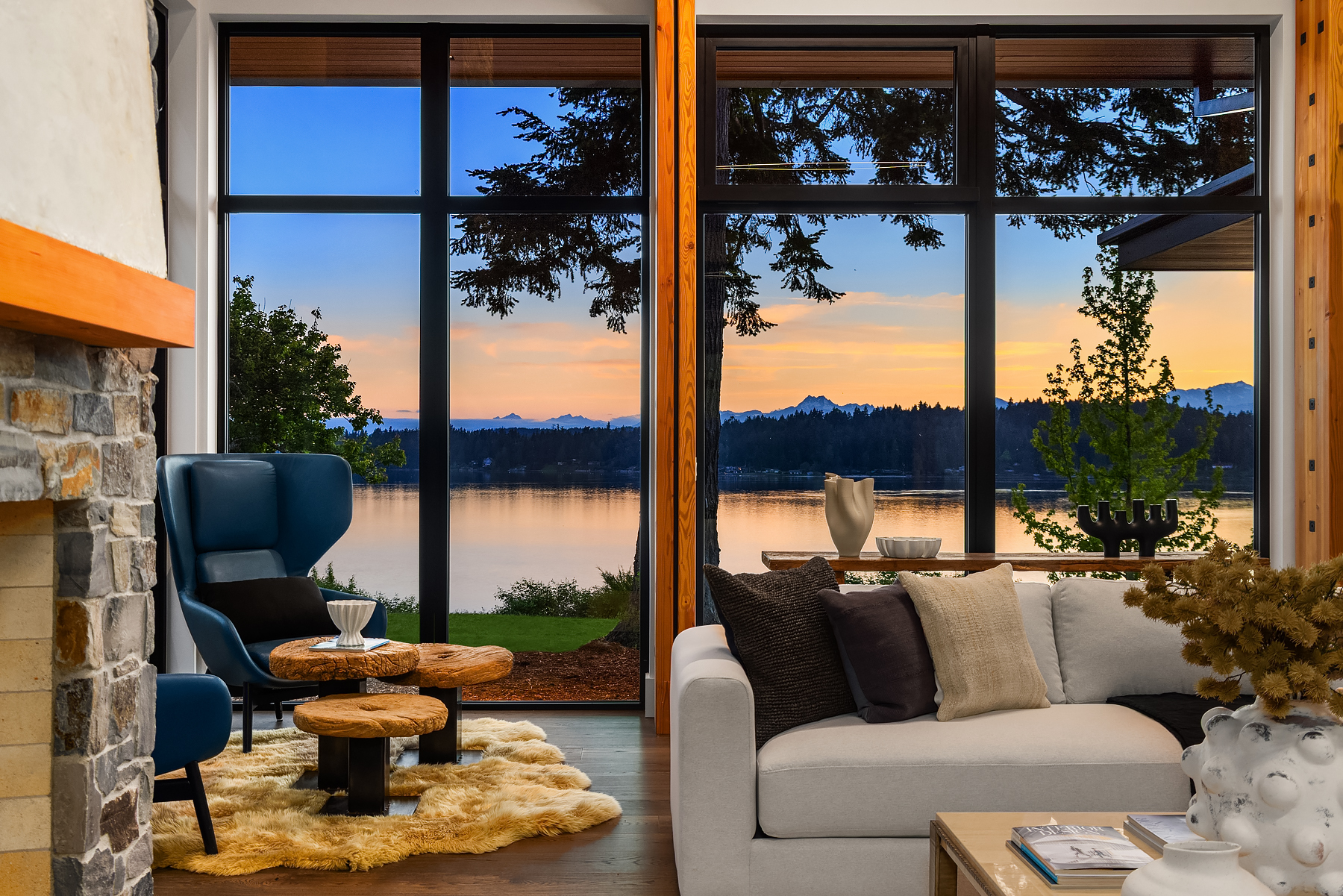 Bainbridge Island waterfront living room staged with ivory seating, a sculptural coffee table, and sunset views through black-framed windows