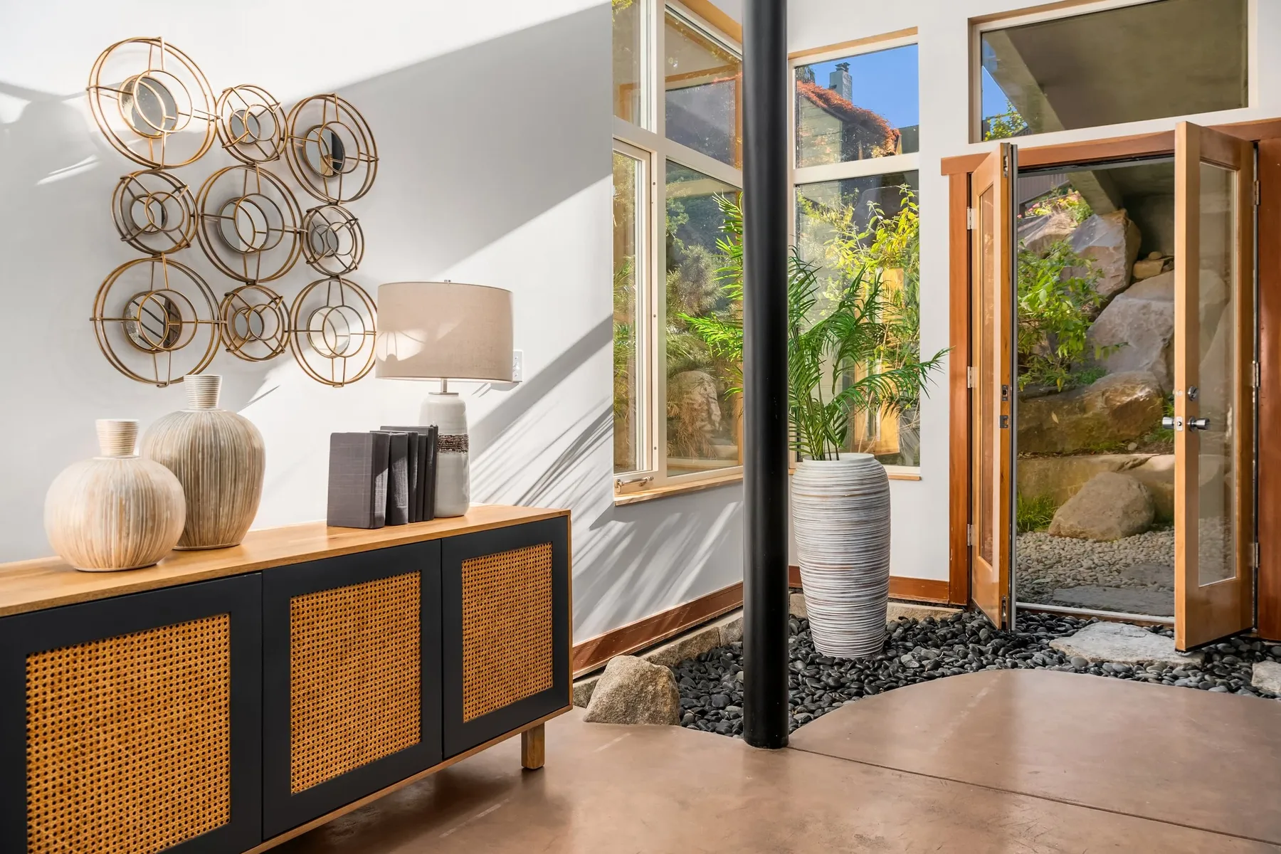 Entry hall staged with a cane-front console, sculptural decor, and glass doors opening to a rock garden