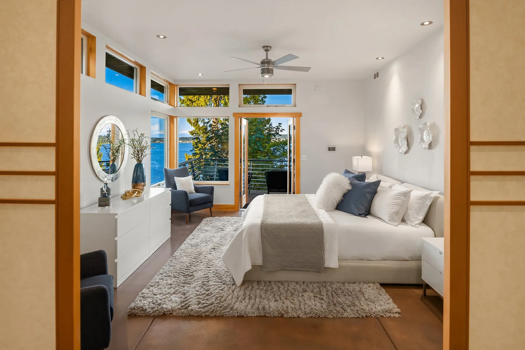 Seattle luxury home staging featuring a serene primary bedroom with a round mirror, layered bedding, and lake views