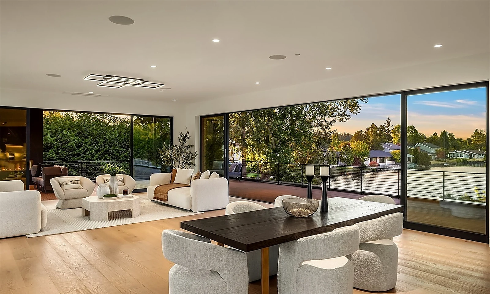 Open living and dining room in a Clyde Hill modern home staged with sculptural white seating and a dark wood dining table beside floor-to-ceiling glass
