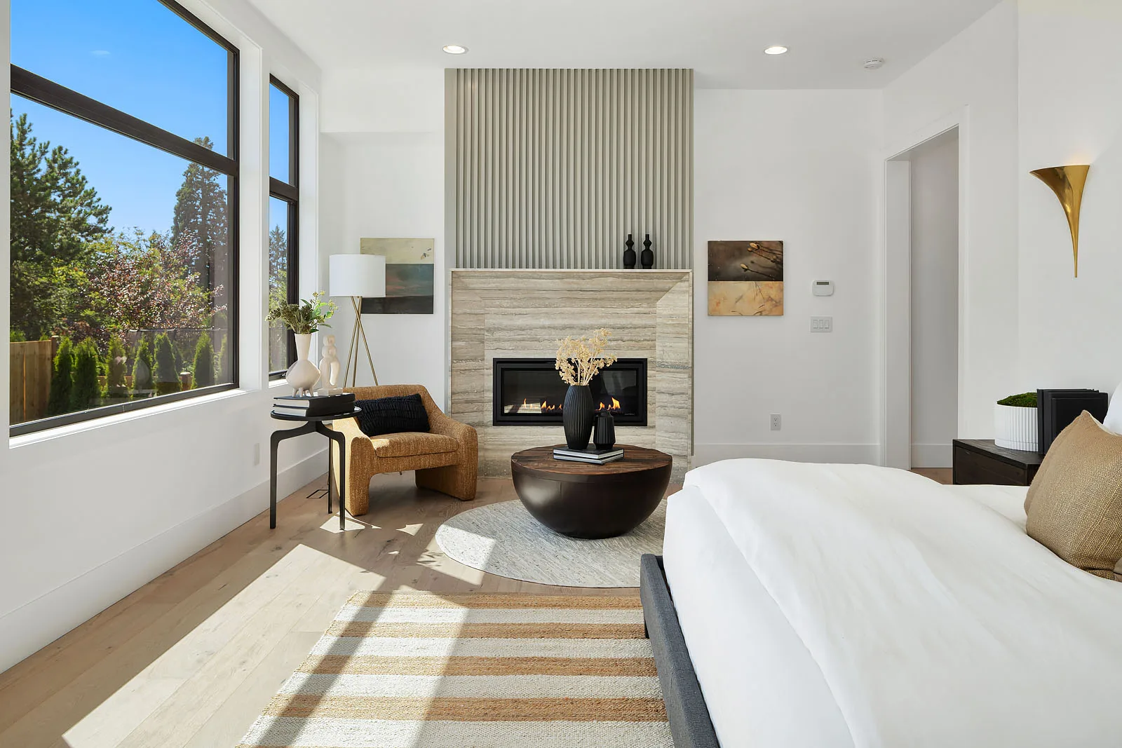 Contemporary Modern primary bedroom with a fluted fireplace, bouclé chair, and large picture windows, staged by RD Interiors