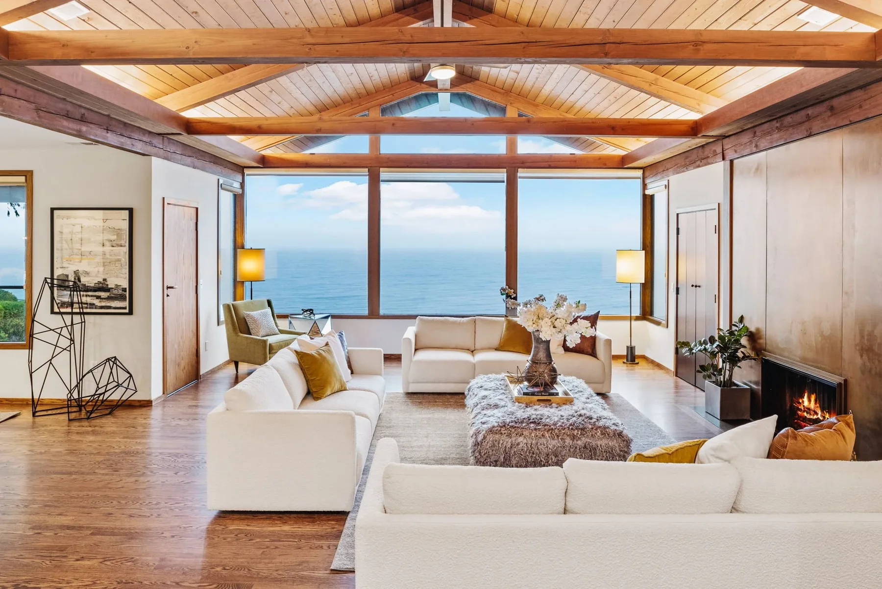 Seattle home staging featuring an open living room with twin sofas, a shag ottoman, and panoramic water views beneath a wood-beamed ceiling