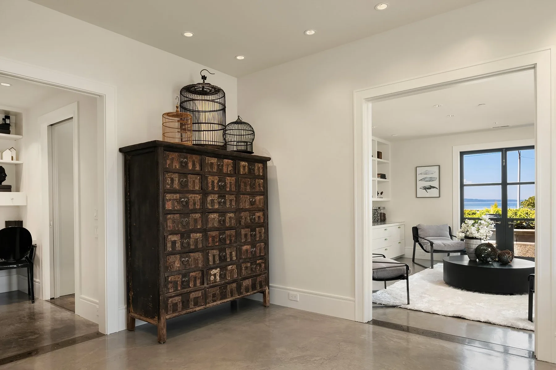 Entry hall staged by RD Interiors with an antique apothecary chest, woven birdcages, and a view into a sitting room over the water