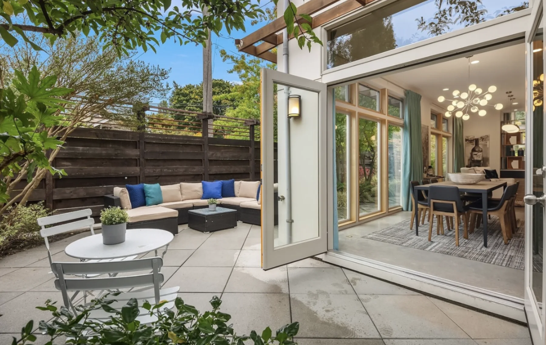 Private garden courtyard staged with an outdoor sectional and bistro set, opening through glass doors to the modern dining room