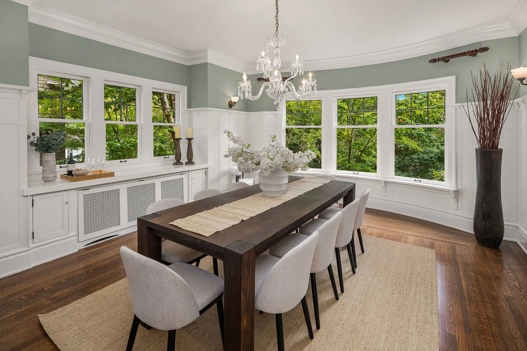 Capitol Hill home staging with a long wood dining table, upholstered chairs, and a glass chandelier against sage-green walls