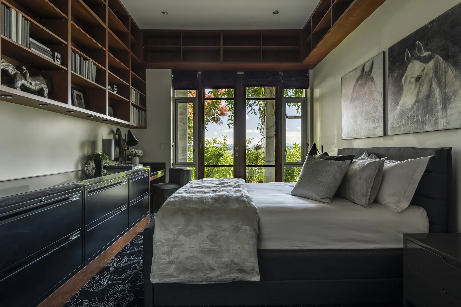 Guest bedroom staged with a dark upholstered bed, equestrian artwork, wood built-in shelving, and French doors to a garden view