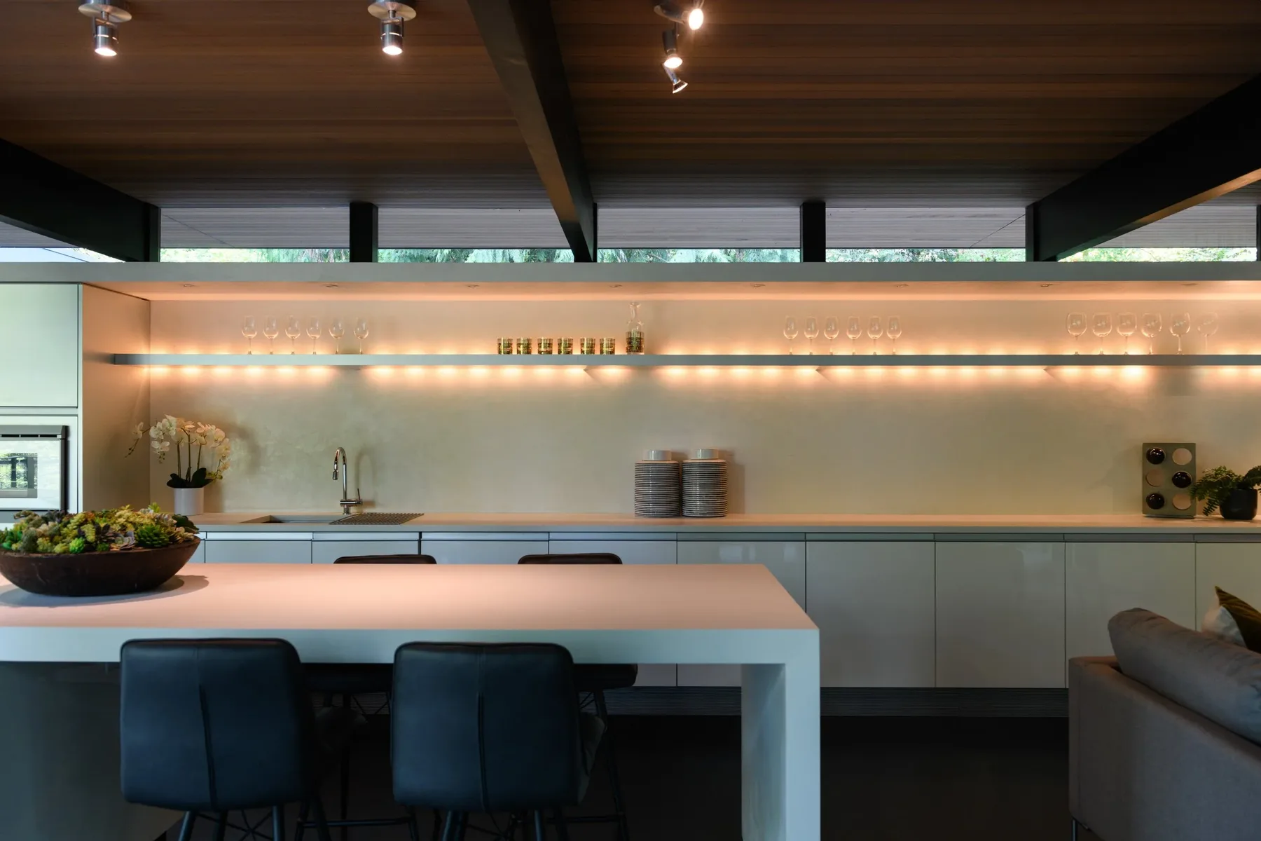 Modern kitchen staged by RD Interiors with a long island, upholstered bar stools, and integrated under-shelf lighting