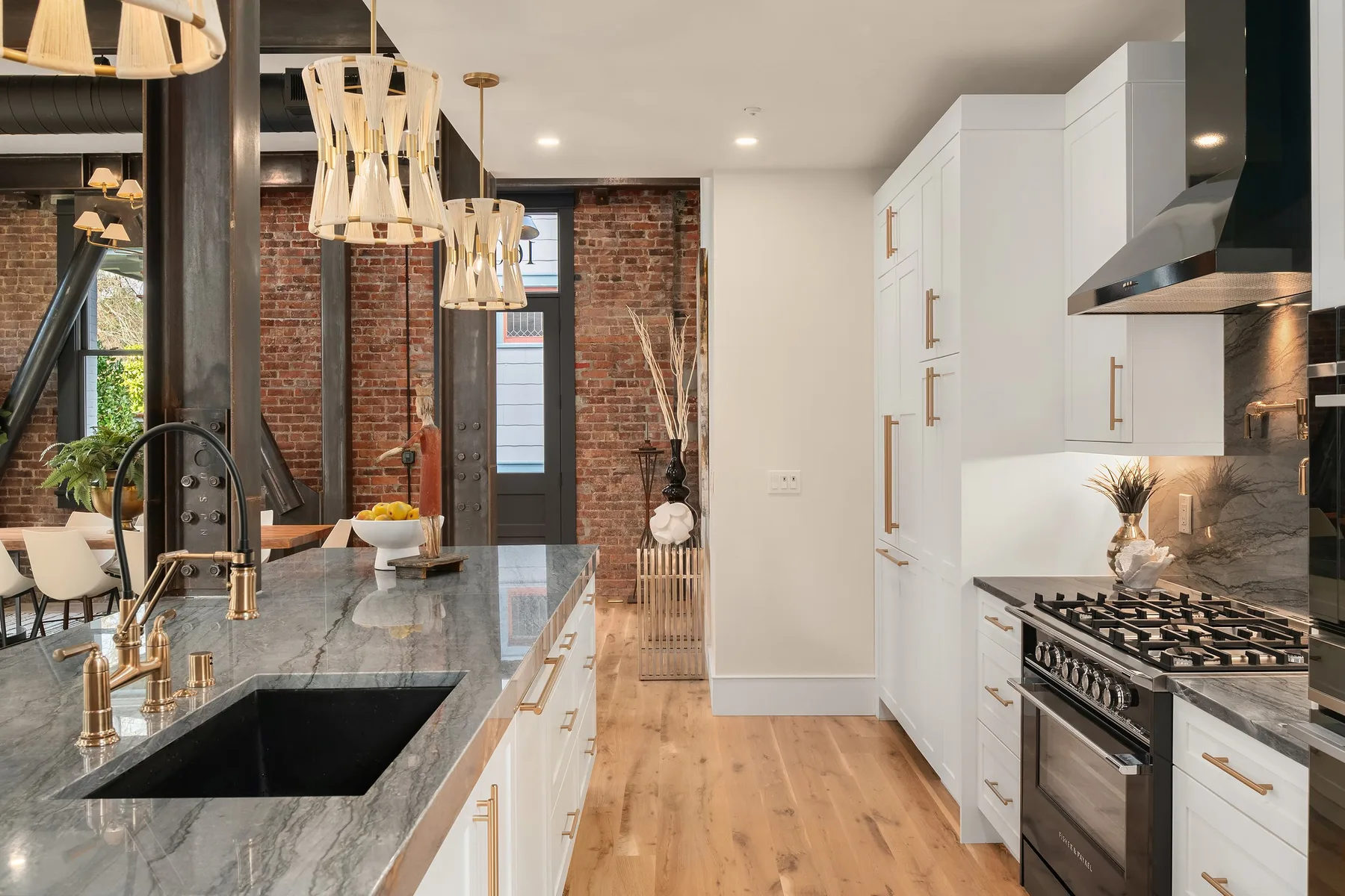Kitchen detail with a marble countertop, undermount sink, brass faucet, and a professional range against exposed brick
