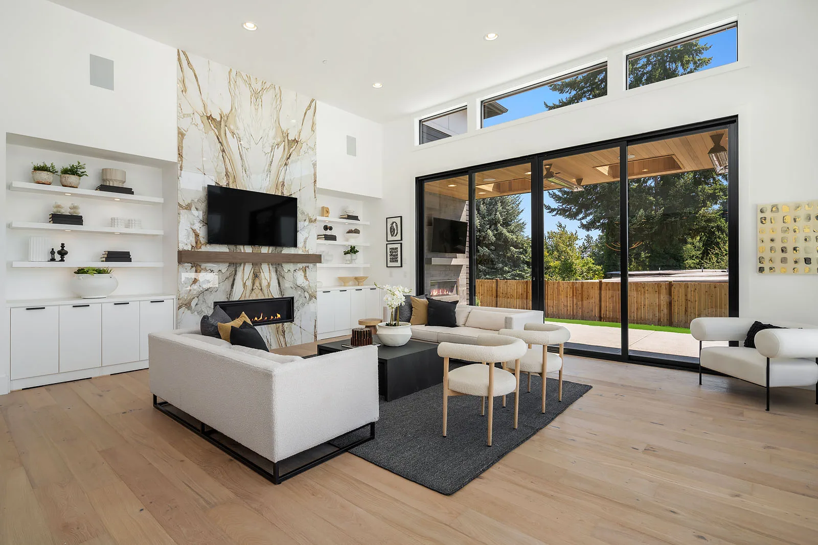 Living room with a dramatic book-matched marble fireplace wall, white bouclé sofas, and a wall of sliding glass doors