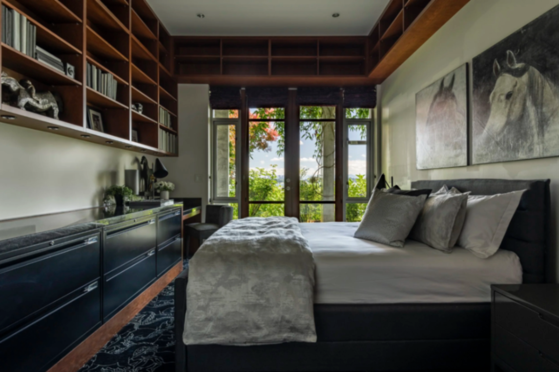 A moody bedroom with built-in shelving, equestrian art, and lush window views staged by RD Interiors