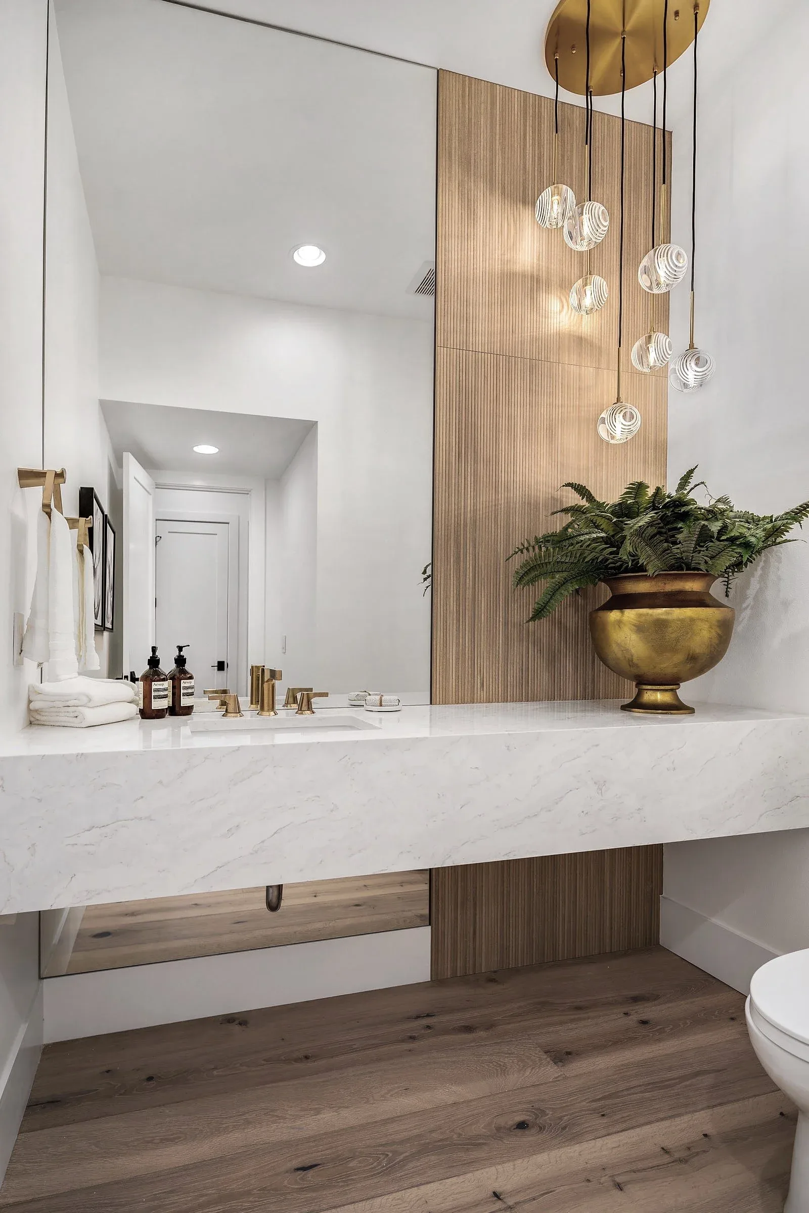 Powder room staged by RD Interiors with a floating marble vanity, walnut accent wall, and cluster pendant lighting