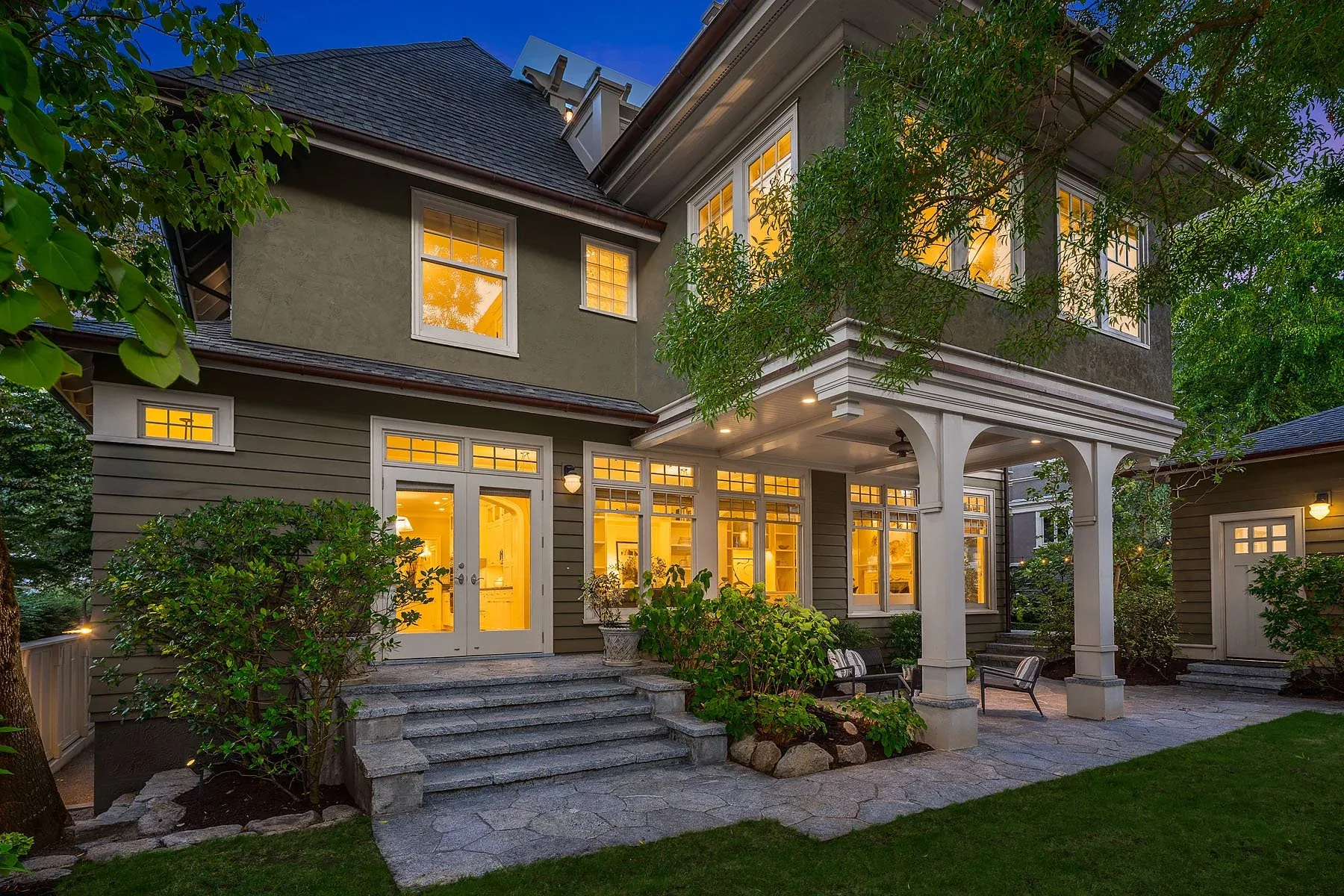 Seattle home staging featuring the rear elevation at twilight with lit French doors, columns, and landscaped grounds
