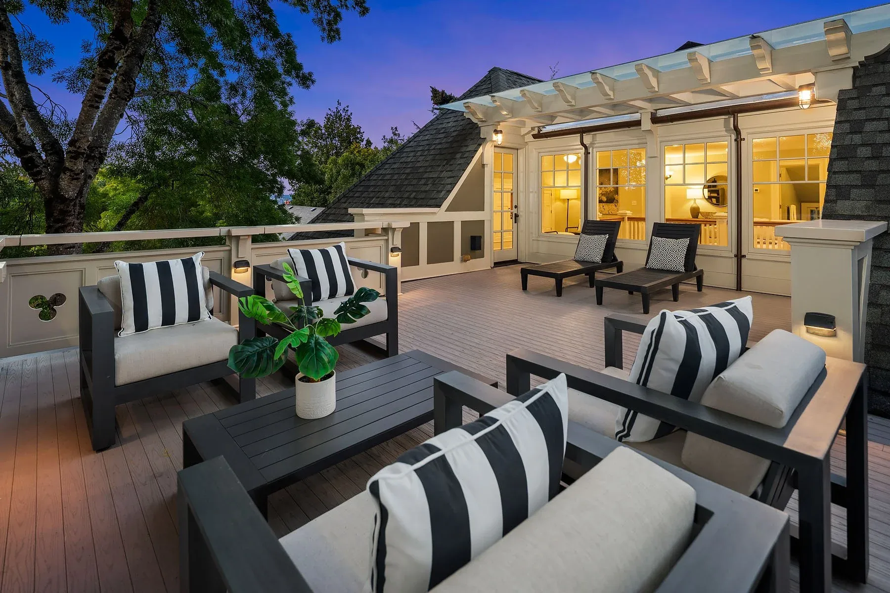 Luxury listing staging featuring a rooftop deck lounge at dusk with black-framed seating and crisp striped cushions