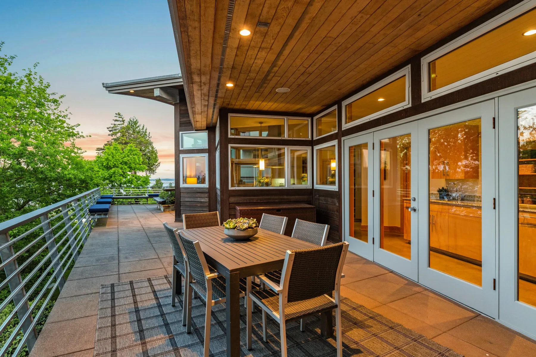 Covered waterfront deck staged with an outdoor dining table beneath a wood ceiling overlooking the lake