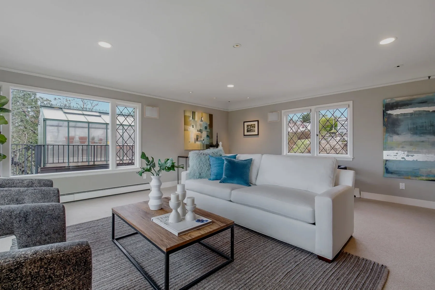 Seattle luxury home staging featuring a family room with a white sofa, gray chairs, leaded glass windows, and moody blue abstract art