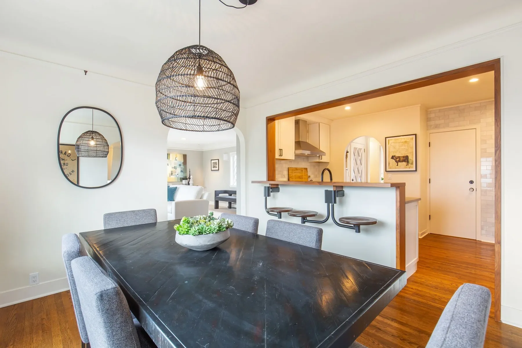 Dining room staged by RD Interiors with a black wood table, gray chairs, a woven pendant, and an opening to the kitchen breakfast bar