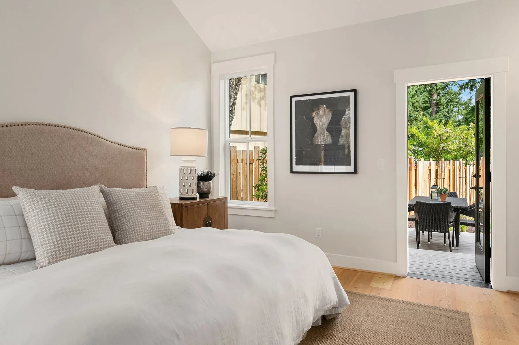 Primary bedroom staged by RD Interiors with an upholstered headboard, neutral linens, and French doors opening to a private deck