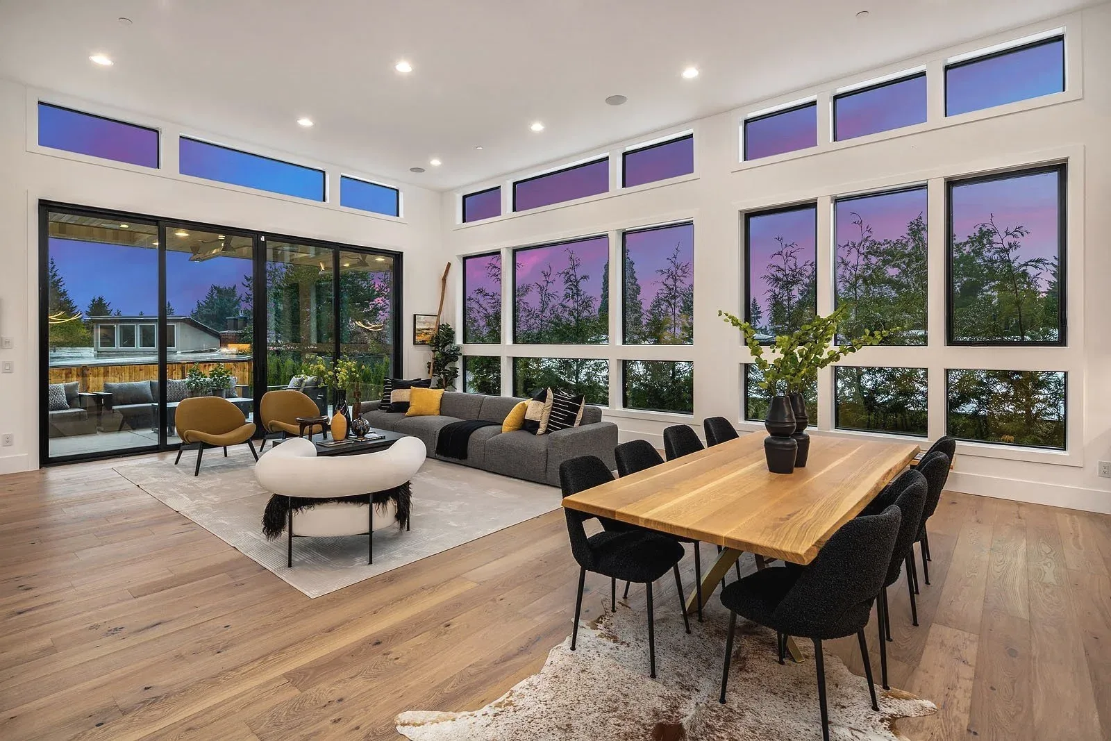 Seattle luxury home staging featuring a modern great room with floor-to-ceiling windows at dusk, a live-edge dining table, and a curved sofa