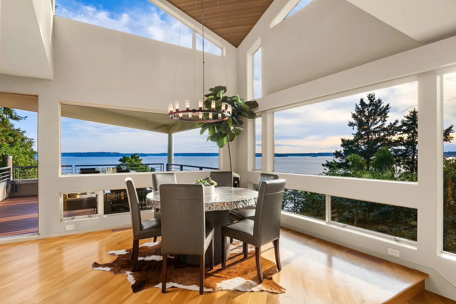 Dining room staged by RD Interiors with a round table, gray upholstered chairs, a cowhide rug, and a vaulted ceiling framing Puget Sound views