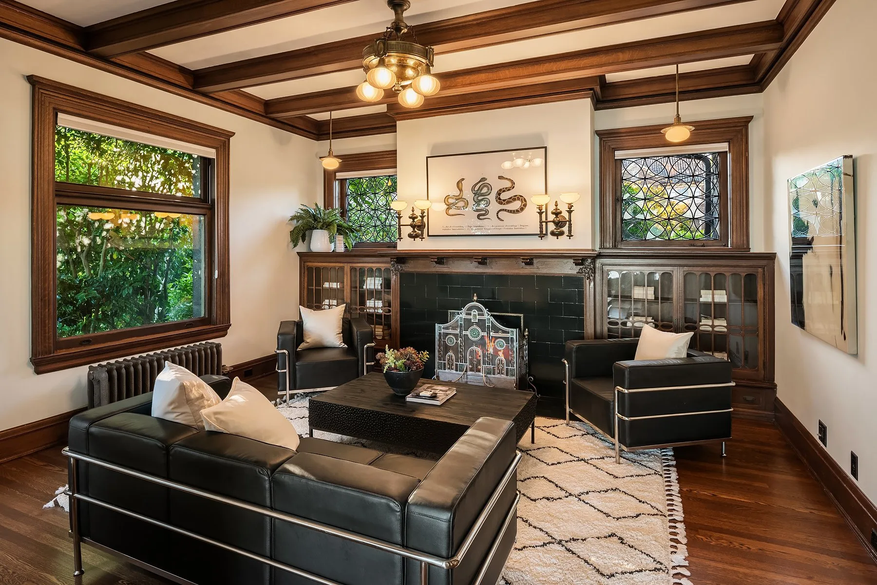 Seattle luxury home staging featuring a paneled sitting room with black leather chairs, a coffered ceiling, leaded windows, and a tiled fireplace