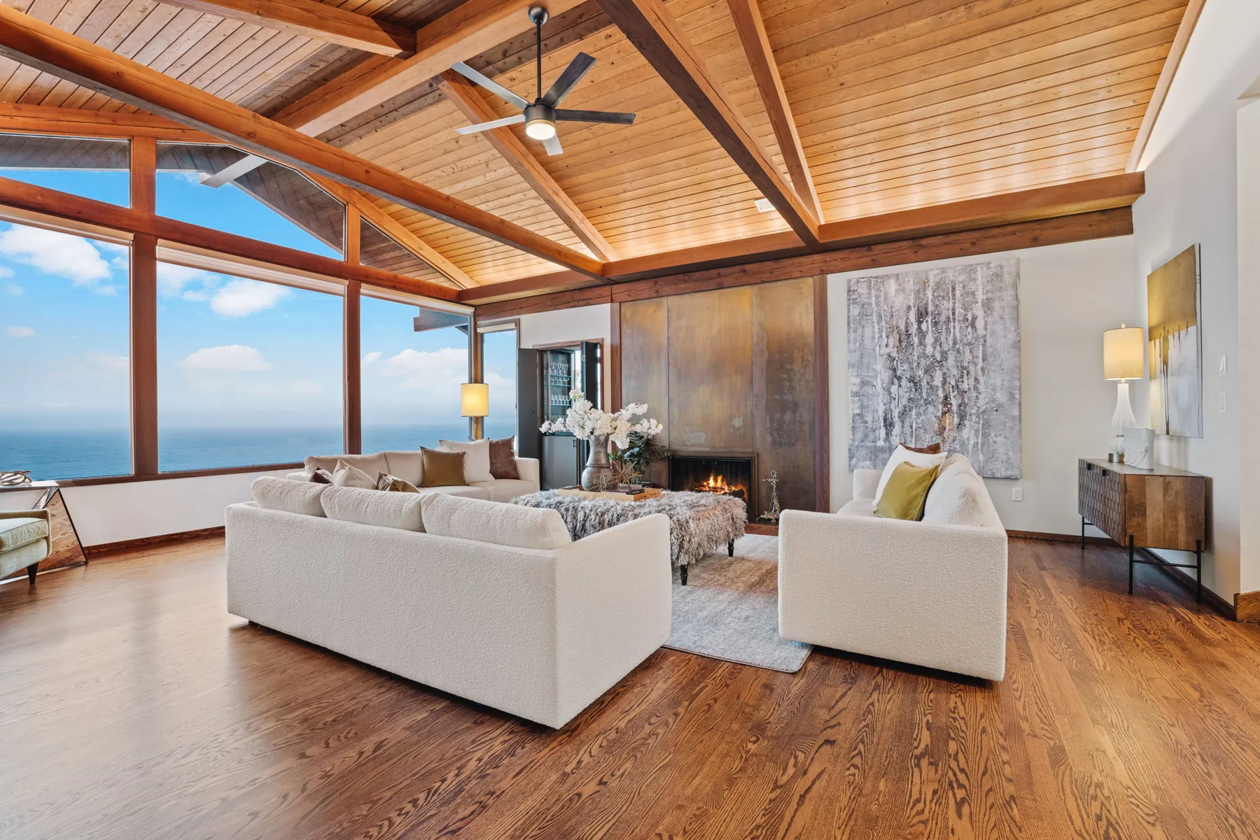 Living room with a fireplace, white sectional sofas, and panoramic windows over the water