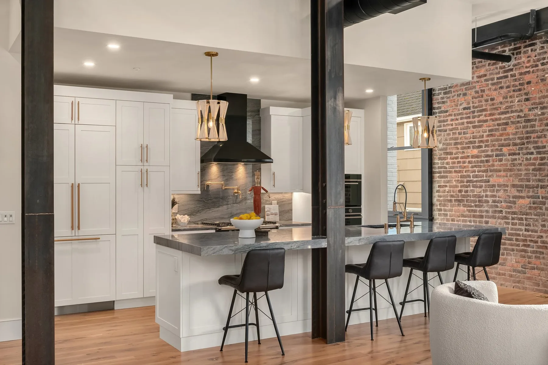 Chef's kitchen with white cabinetry, a grey marble waterfall island, brass fixtures, and upholstered bar stools