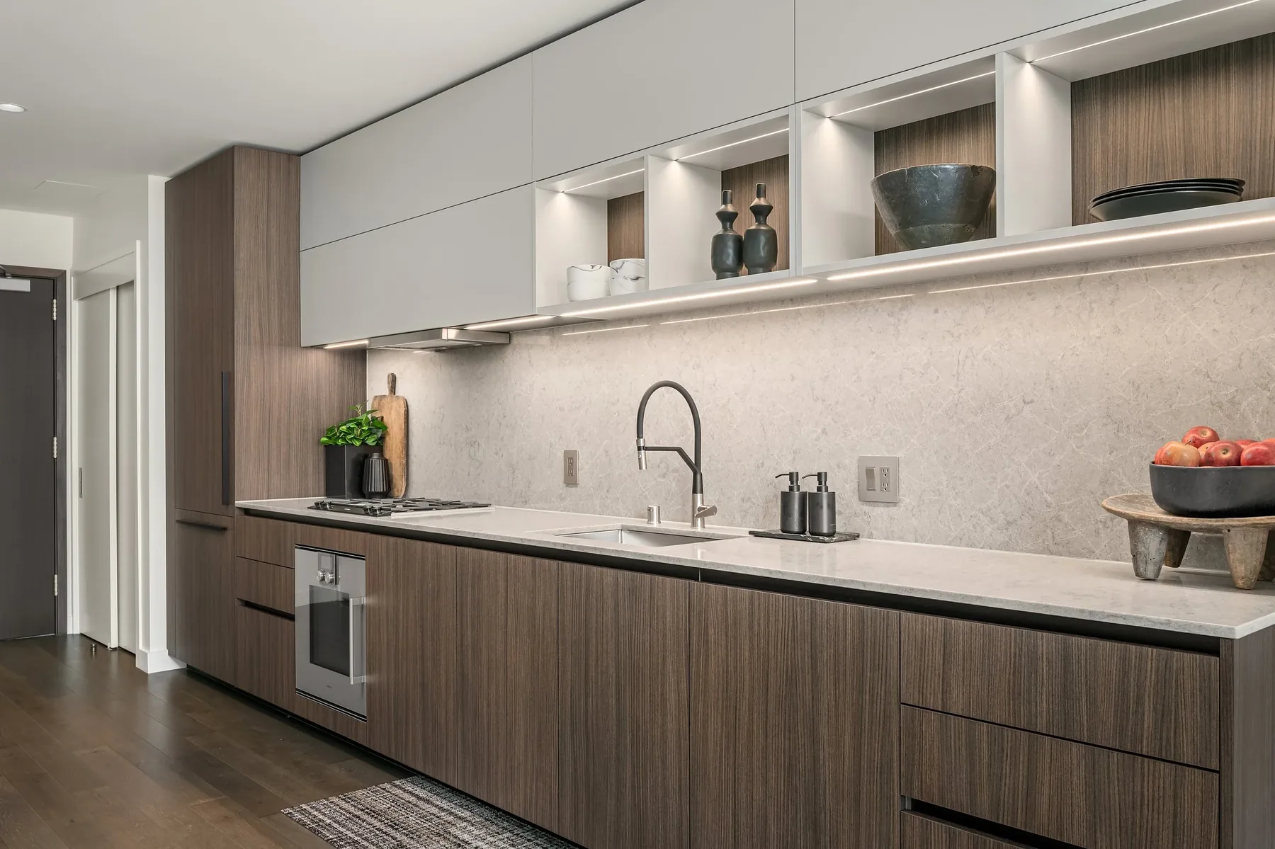 Modern condo galley kitchen staged with walnut cabinetry, a stone backsplash, and refined countertop styling