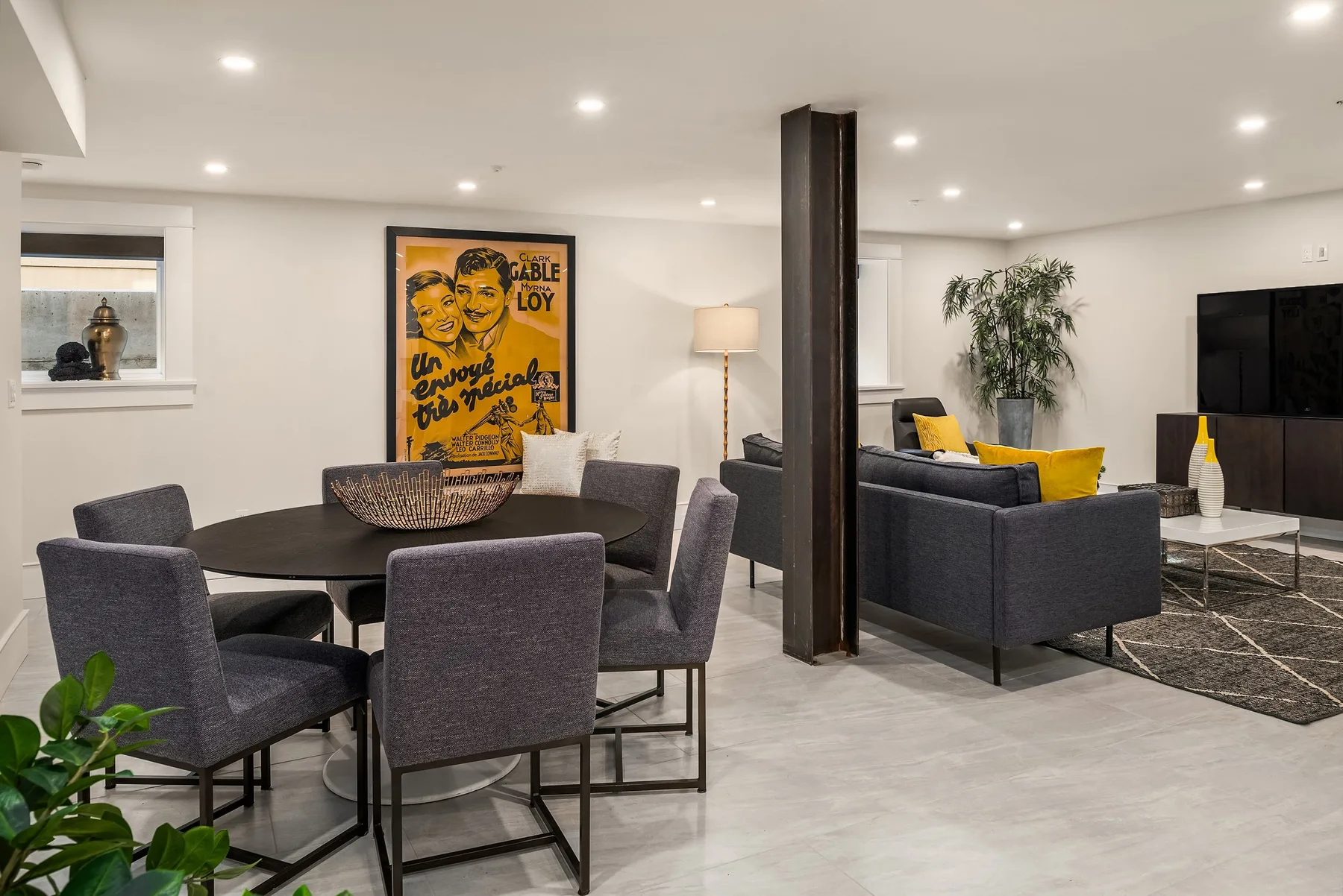 Lower-level lounge staged with charcoal dining chairs, a sectional sofa, and vintage poster art
