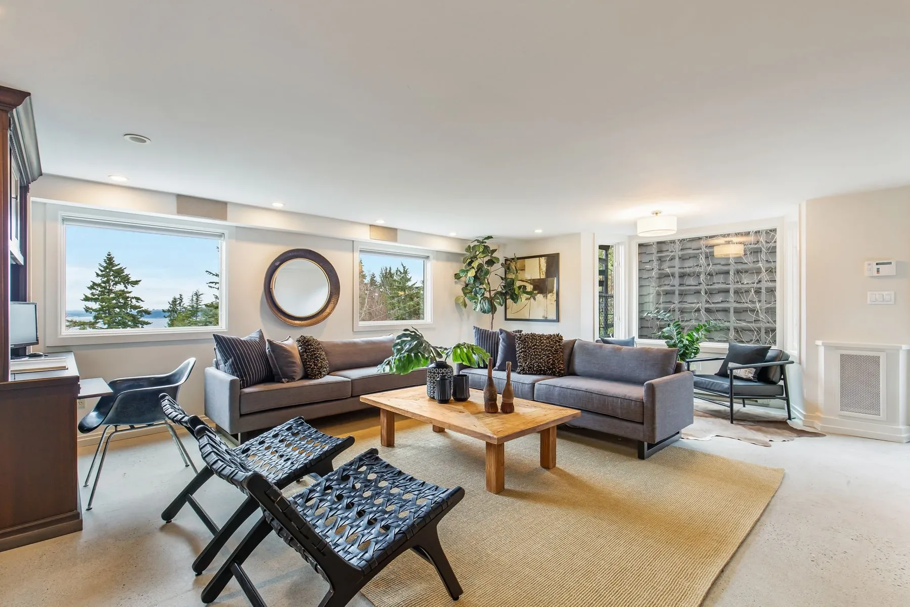 Lower-level living room staged with gray sofas, a round mirror, a wood coffee table, and windows framing the water view
