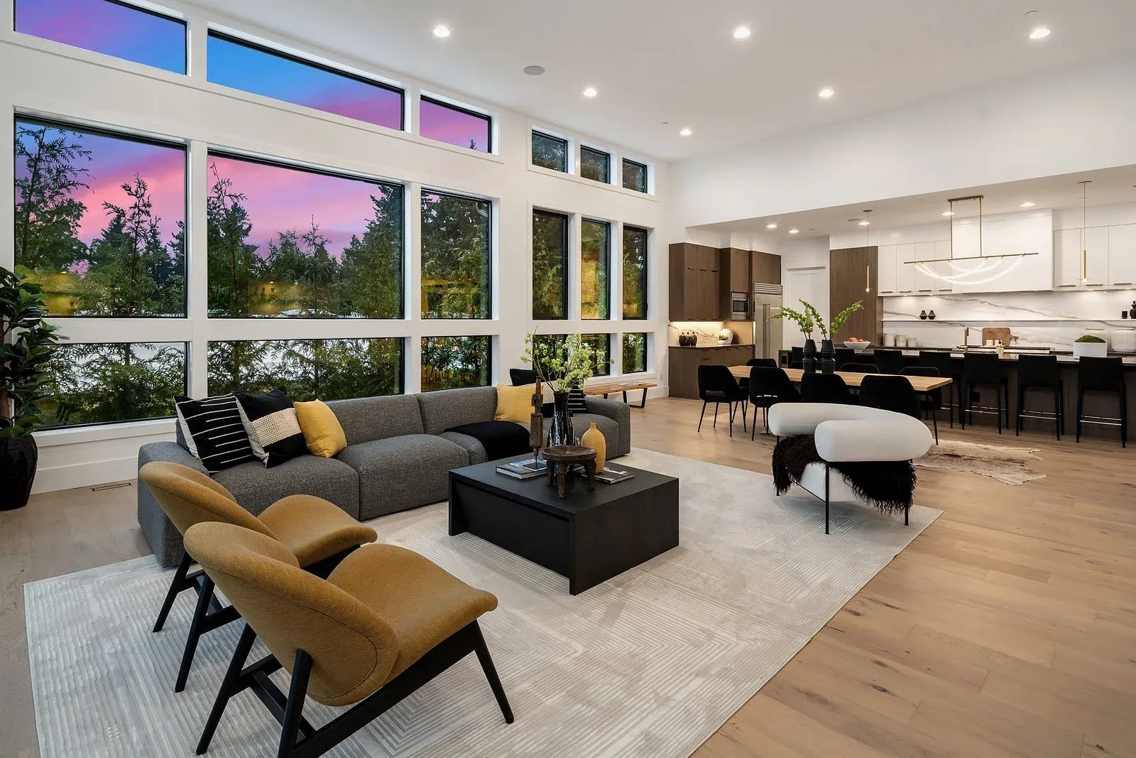 Seattle luxury home staging with an open living lounge, mustard accent chairs, and views over the treetops at dusk
