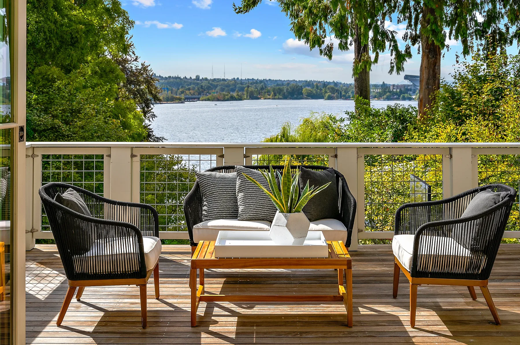 Waterfront deck staged by RD Interiors with black rope lounge chairs, a wood coffee table, and a railing overlooking the lake
