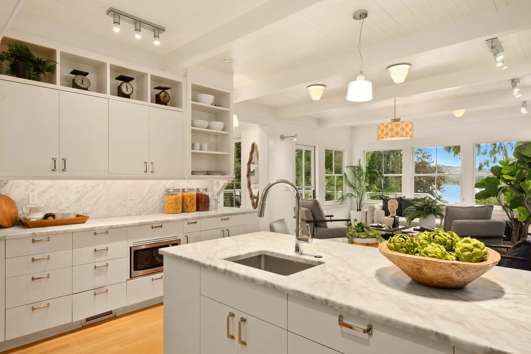 Kitchen staged by RD Interiors with white cabinetry, a marble island, open shelving, and a sitting area with lake views beyond