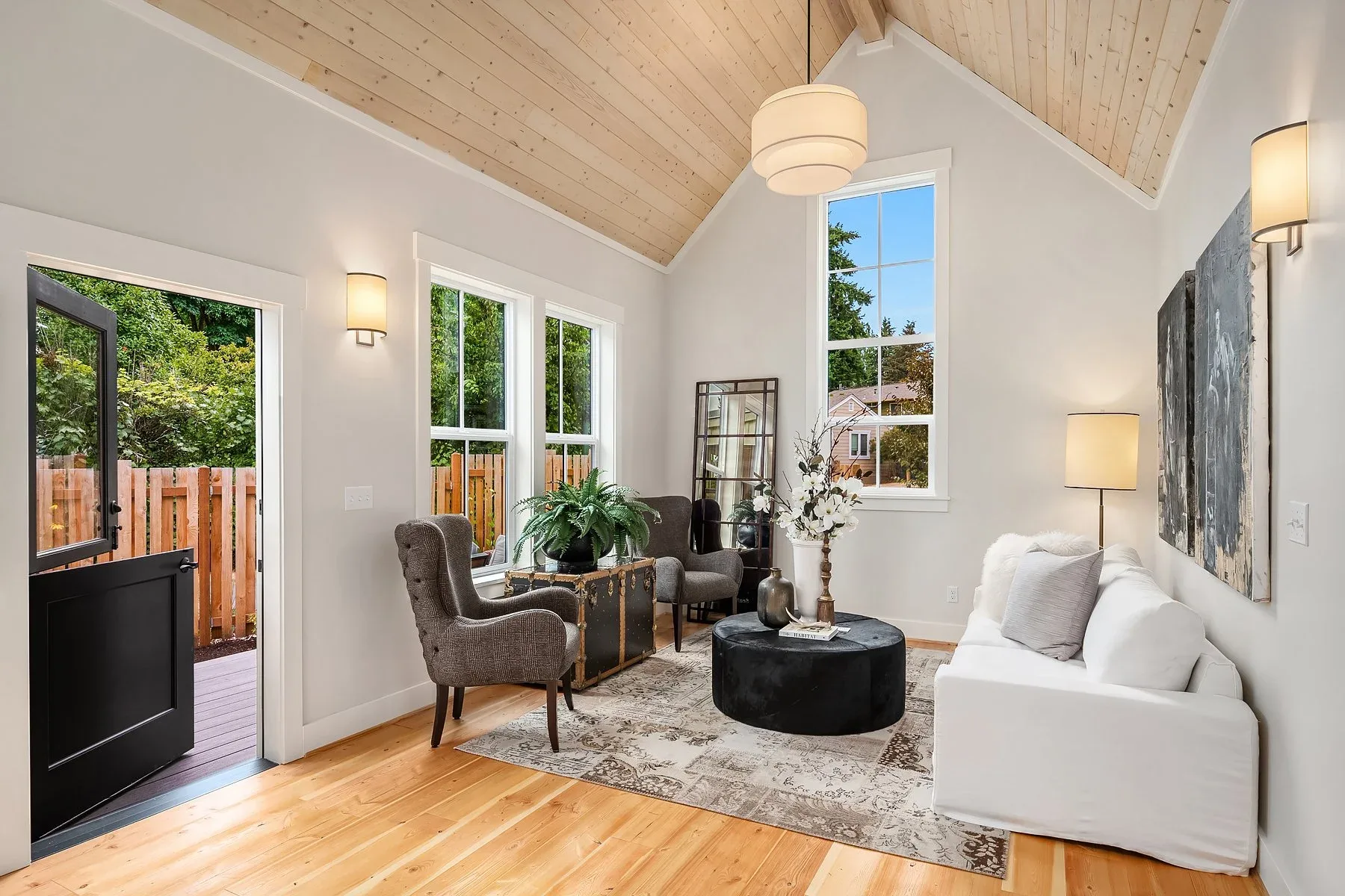 Living room staged with a white slipcovered sofa, tufted accent chairs, an antique trunk table, and a vaulted cedar ceiling