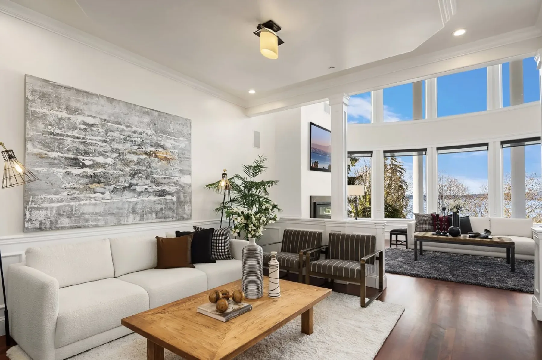 Living room staged by RD Interiors with a bouclé sofa, large abstract art, a wood coffee table, and walls of windows framing the water