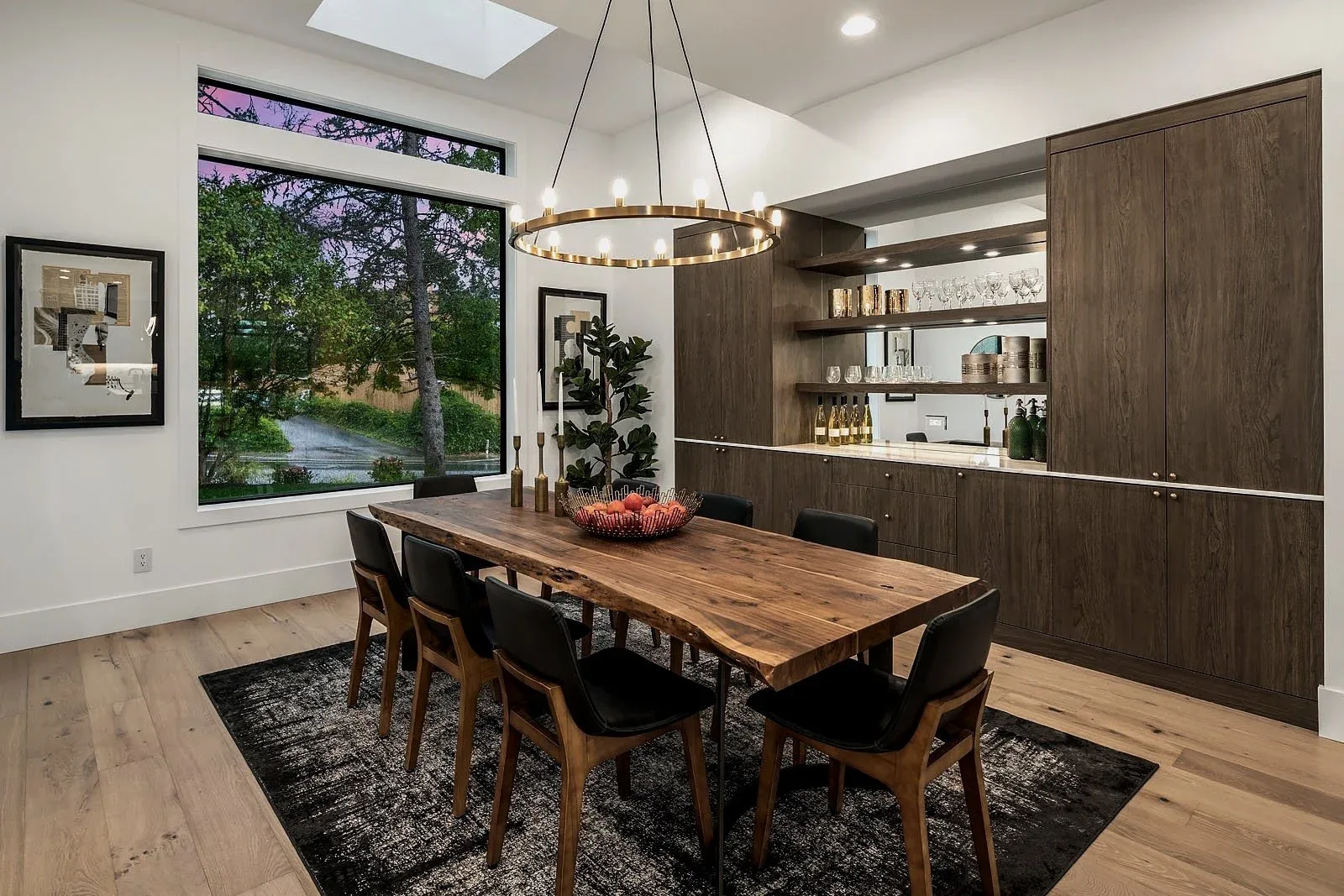Modern dining room staged with a wood table, sculptural chandelier, and a built-in walnut bar against bright windows