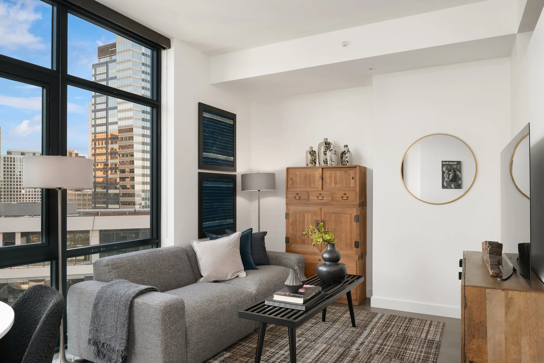 Luxury home staging in Seattle featuring a downtown living room with a grey sofa, walnut cabinet, and panoramic high-rise views