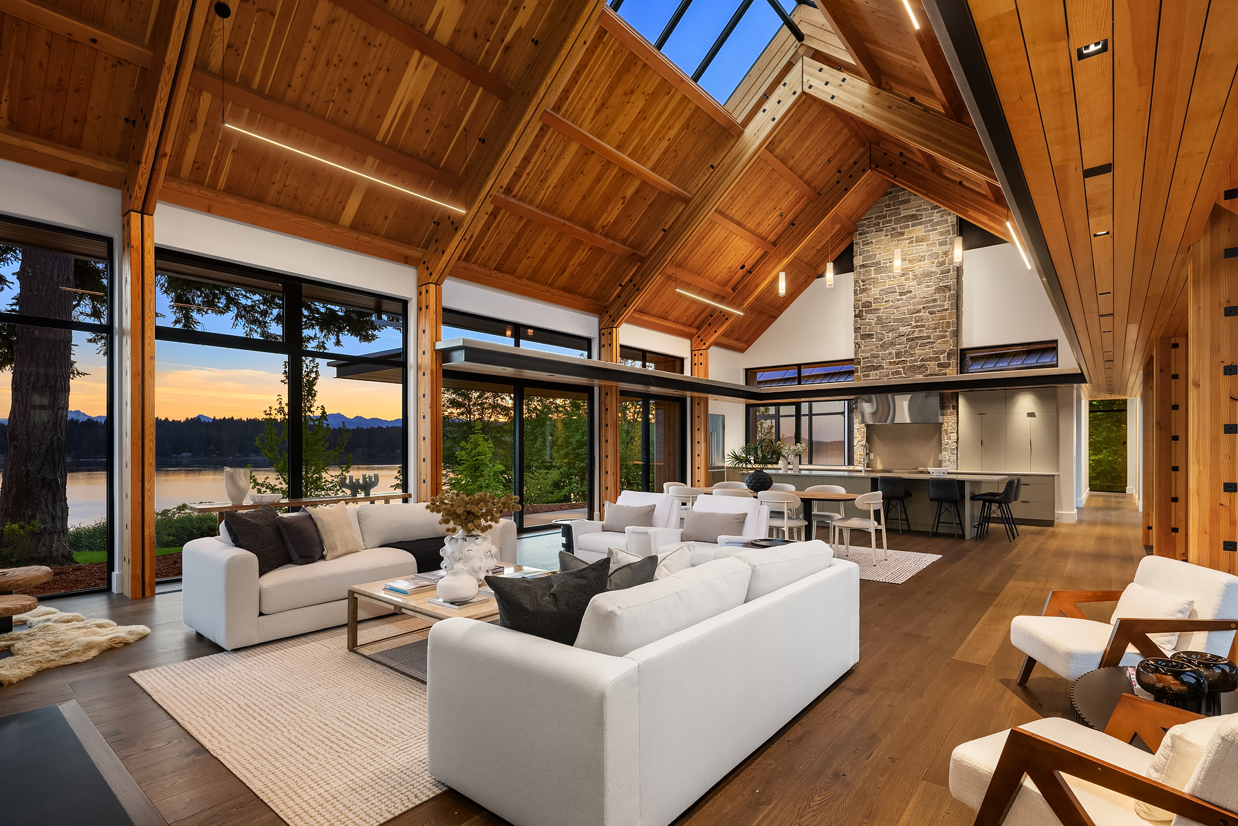 Twilight great room with cedar ceiling detail, staged lounge seating, and an open kitchen facing the water
