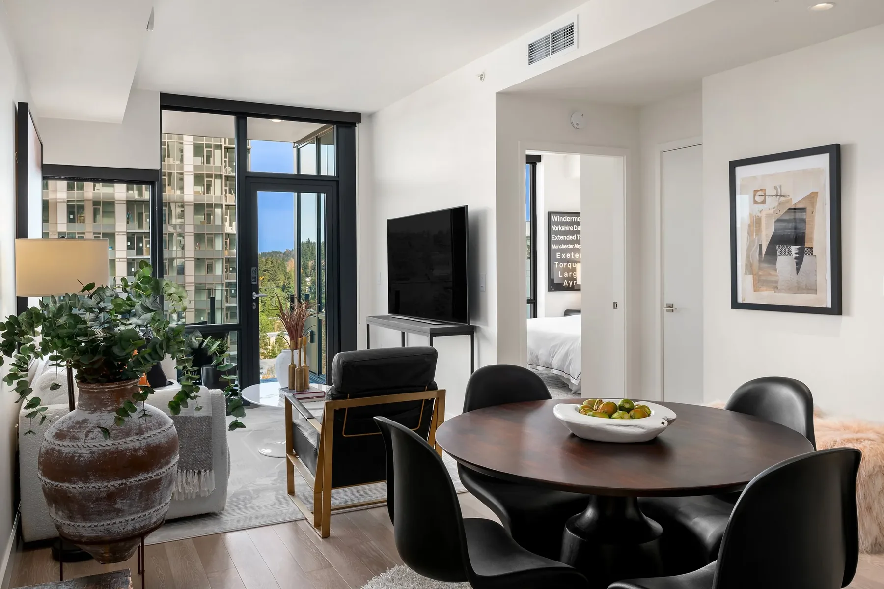 Seattle luxury home staging featuring a high-rise living and dining room with greenery, a media wall, and balcony views of the skyline
