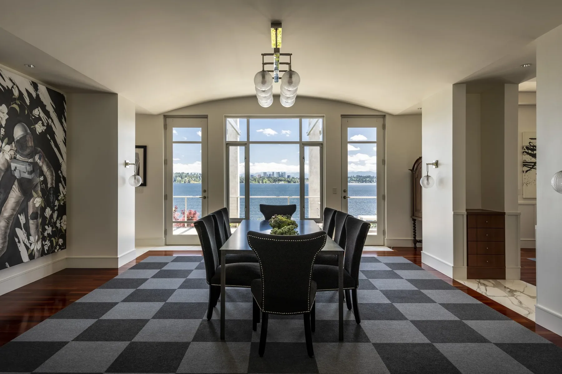 Dining room staged with a dark wood table, black nailhead chairs, large astronaut artwork, and a barrel ceiling above lake-view windows
