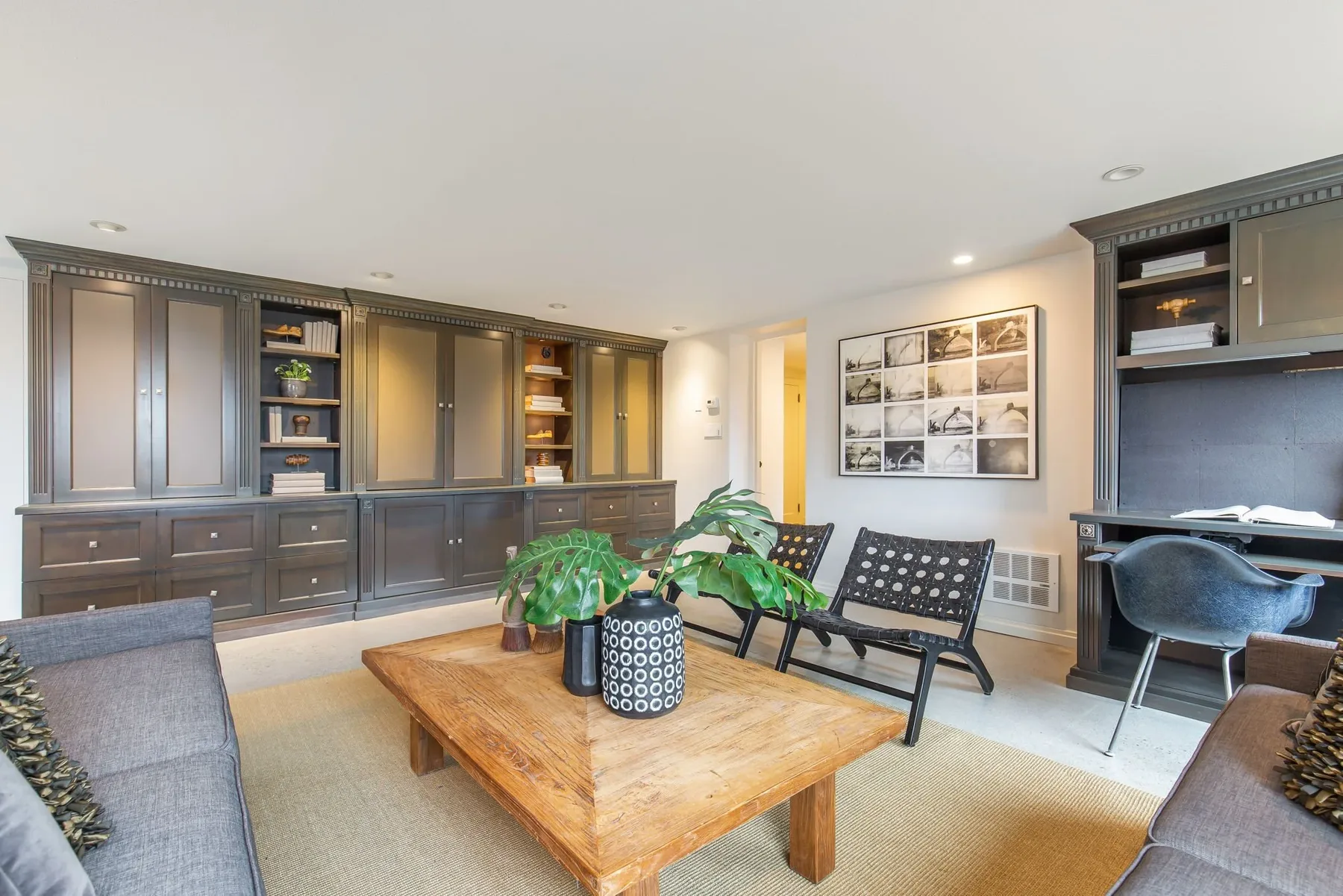 Den staged by RD Interiors with built-in cabinetry, a gray sofa, woven leather chairs, and a rustic wood coffee table