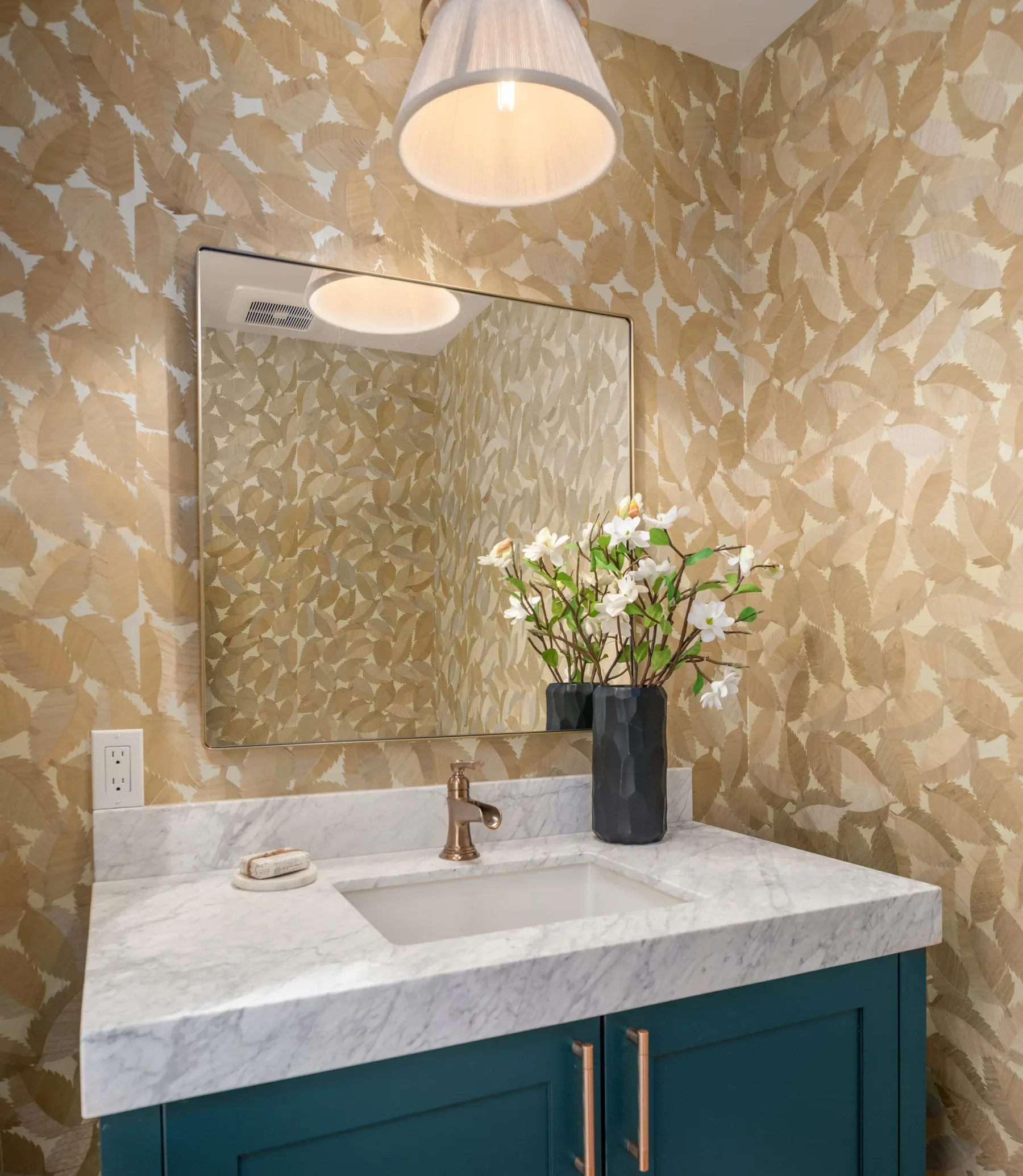 Powder room with textured gold wallpaper, a marble-topped vanity, and brass fixtures