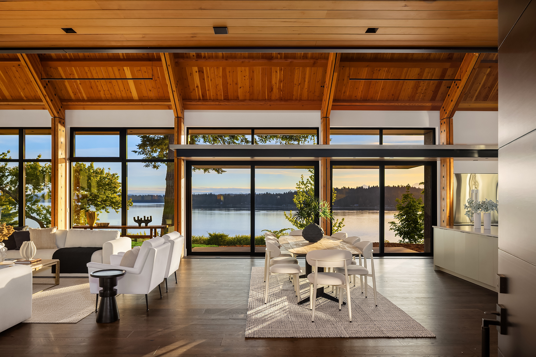 Dining area staged beside floor-to-ceiling glass with calm waterfront views and warm evening light