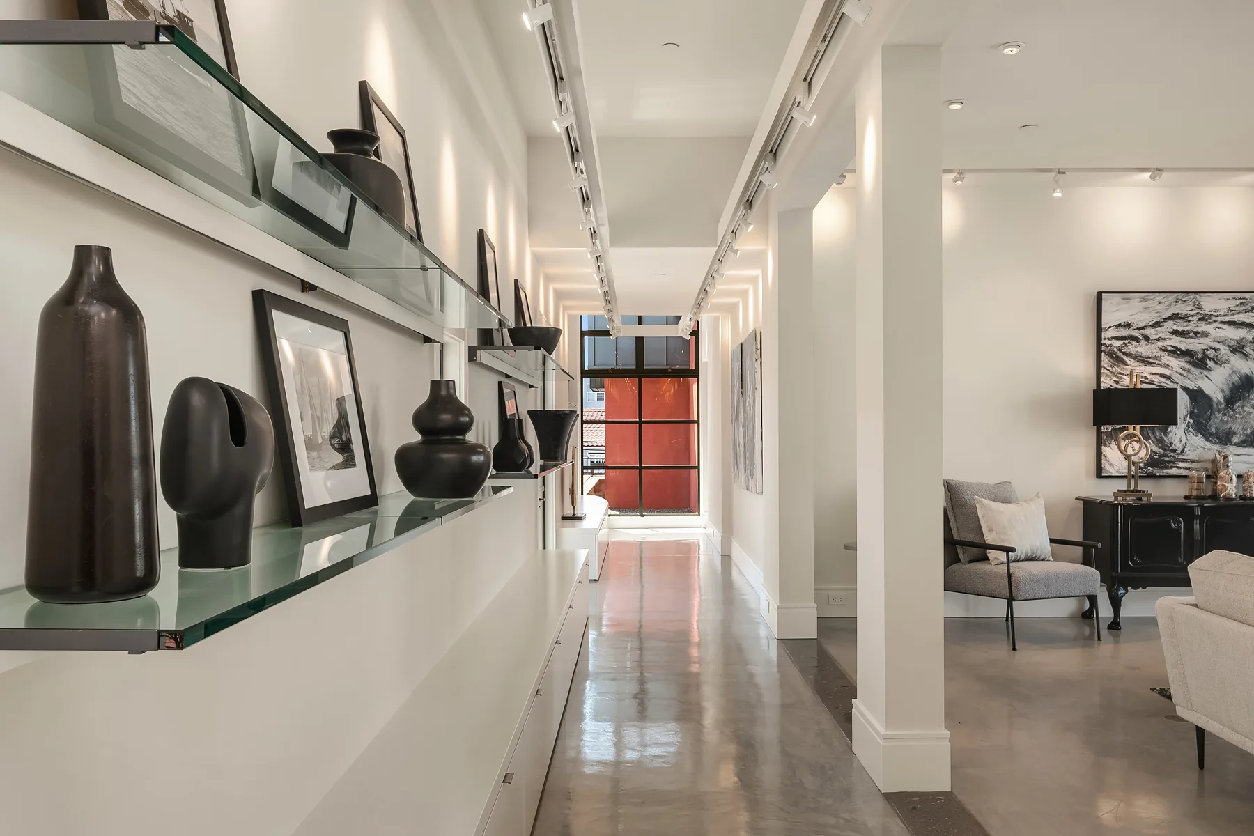 Gallery hallway with floating glass shelves, sculptural objects, and polished concrete floors