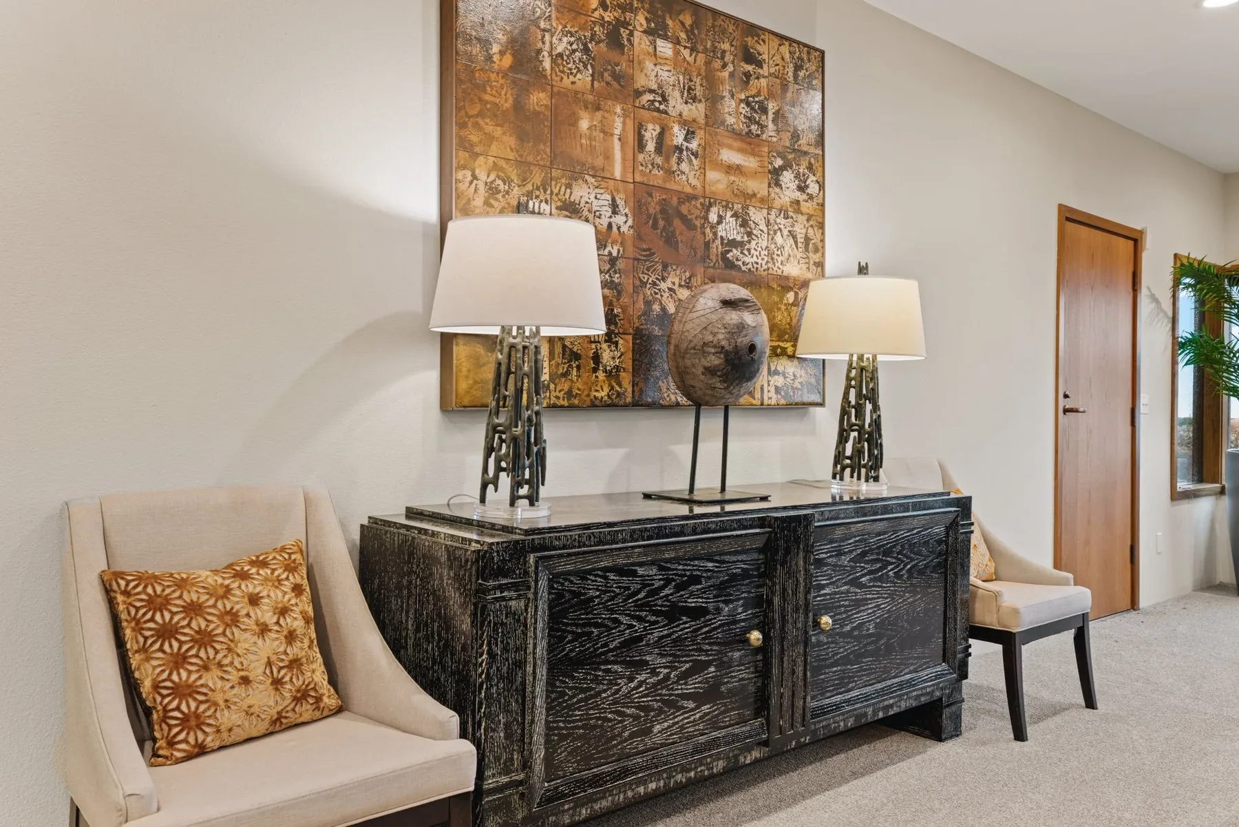 Sitting nook staged with a dark wood console, twin lamps, large-scale art, and a pair of accent chairs