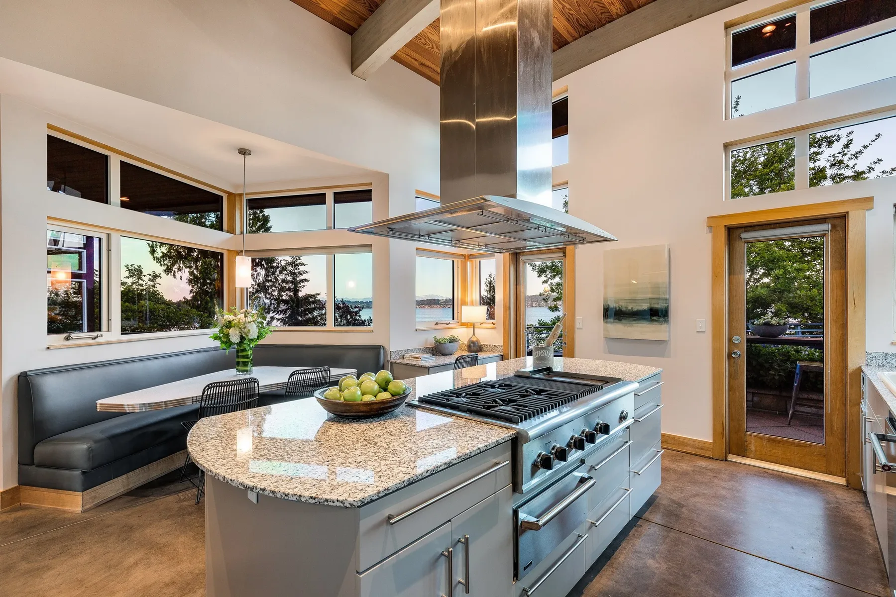 Seattle luxury home staging featuring a chef's kitchen with a granite island, statement range hood, and a window banquette over the water