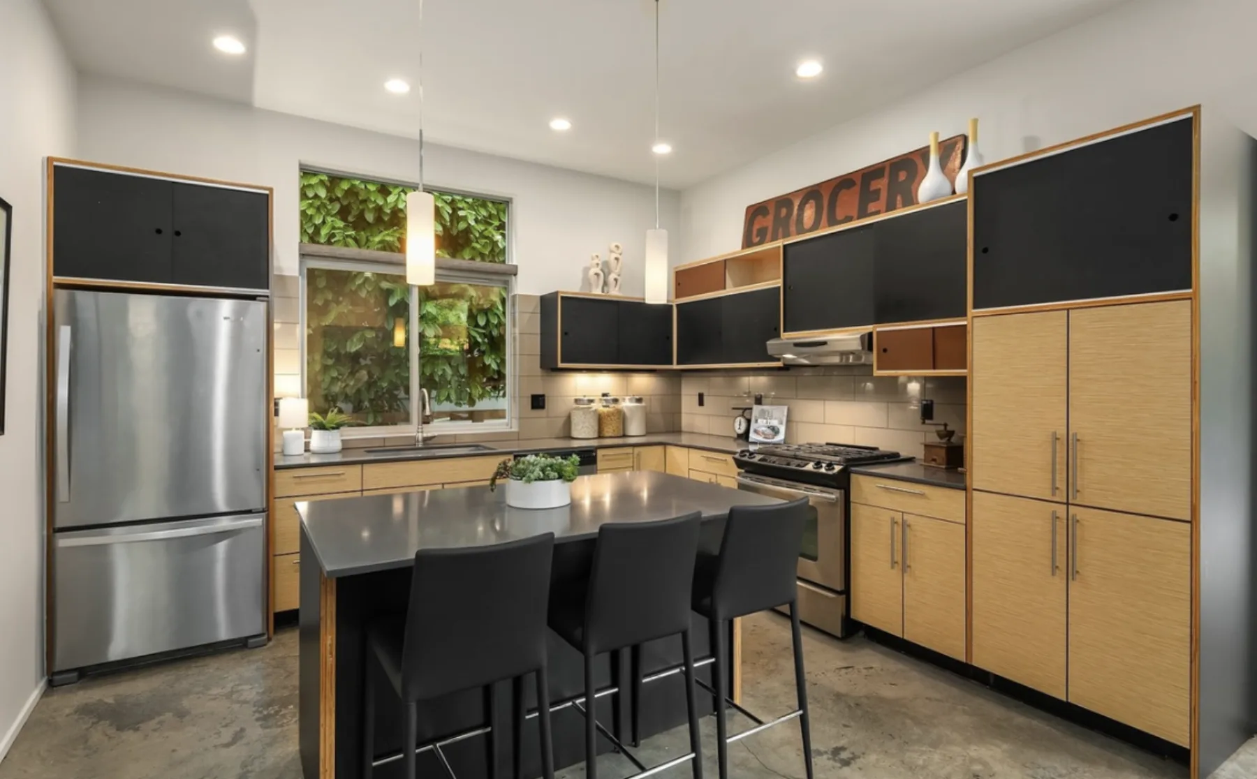 Modern kitchen staged by RD Interiors with wood and black cabinetry, a concrete-topped island, and black bar stools