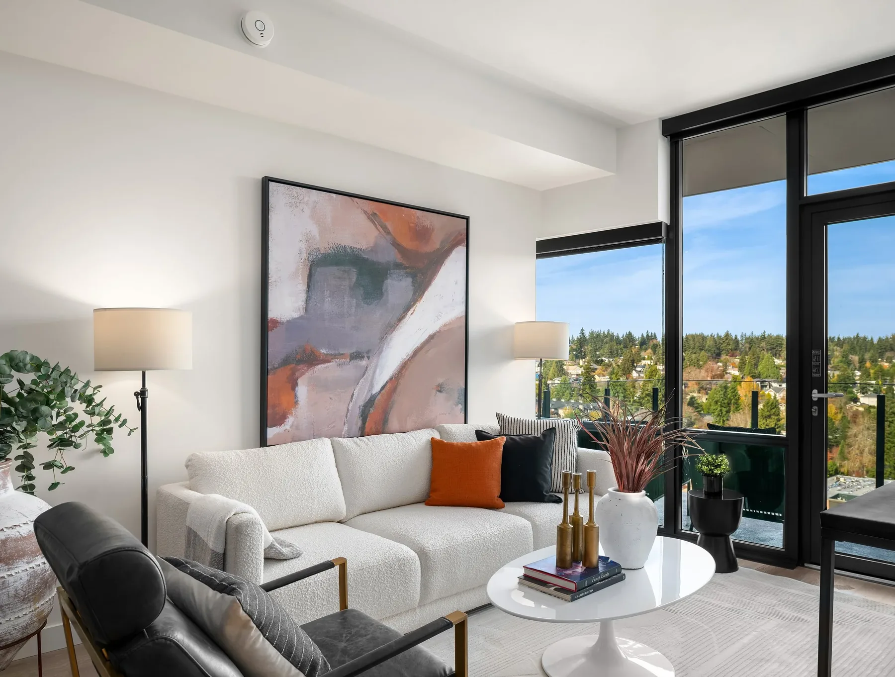 Seattle luxury home staging with a bright high-rise living room, neutral sofa, abstract canvas, and floor-to-ceiling windows over the treetops