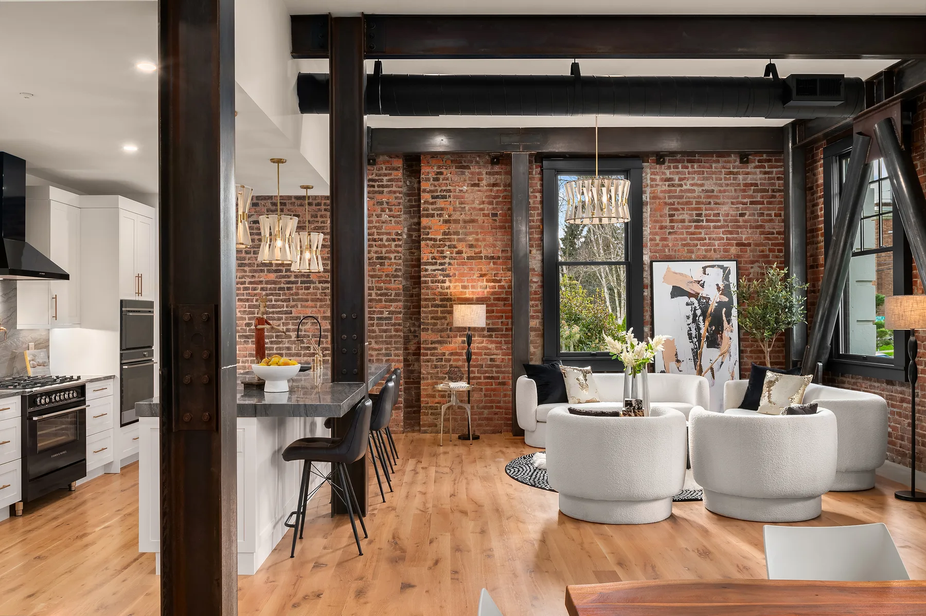 Open-concept great room blending the kitchen and living areas beneath original brick and steel