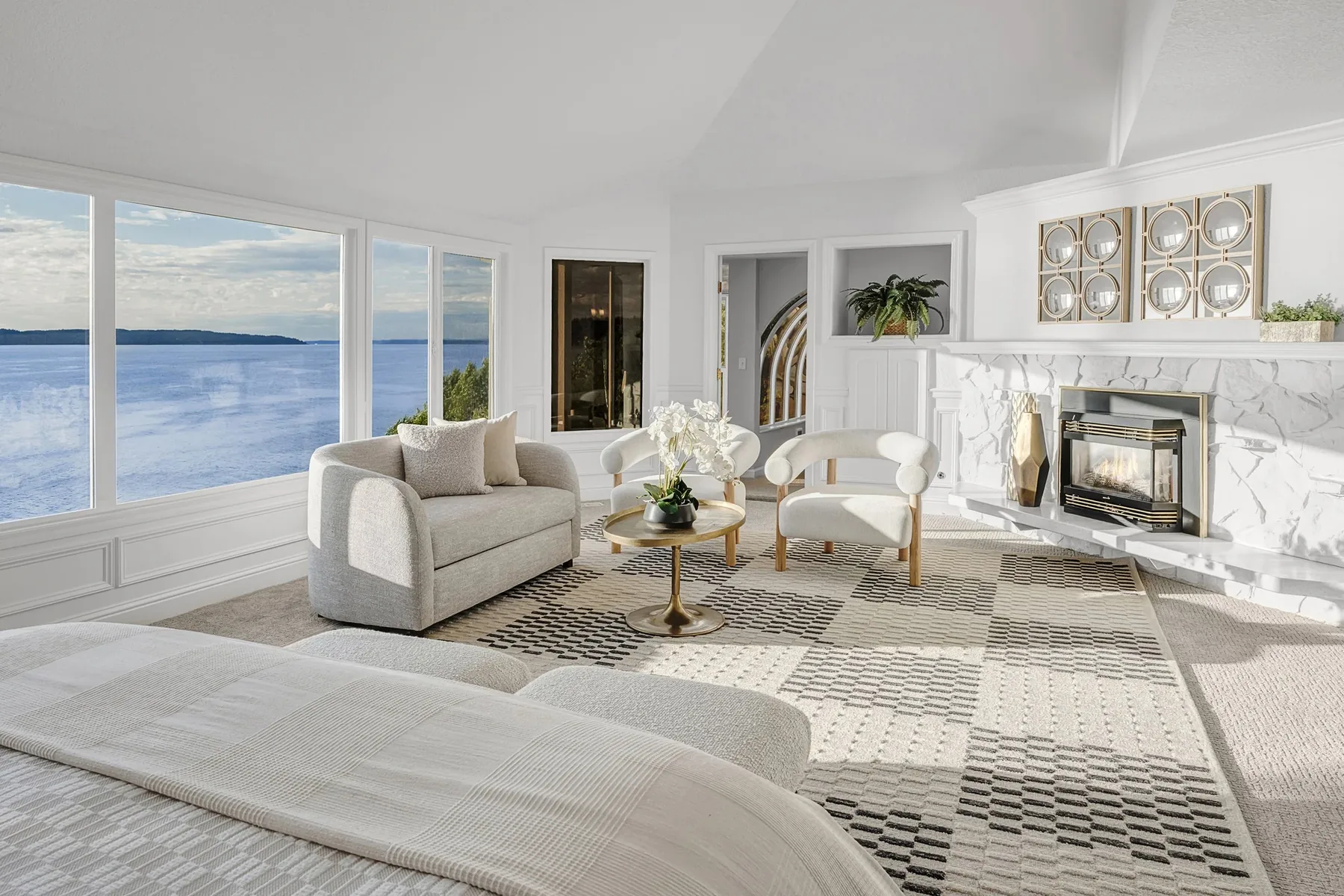 Waterfront home staging with a fireside living room, marble fireplace, curved sofa, and panoramic water views for a market-ready presentation