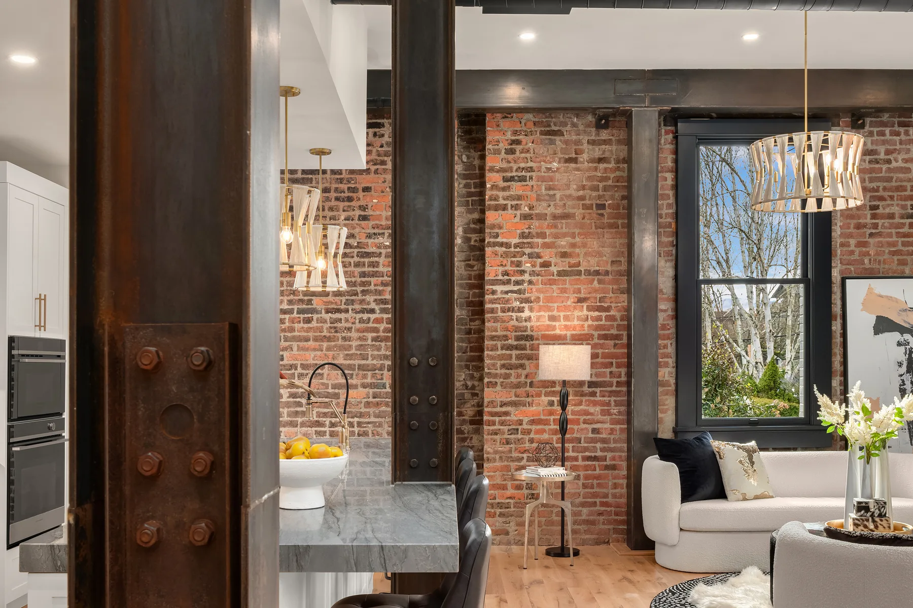 Riveted steel column detail framing the kitchen and brick-walled living area